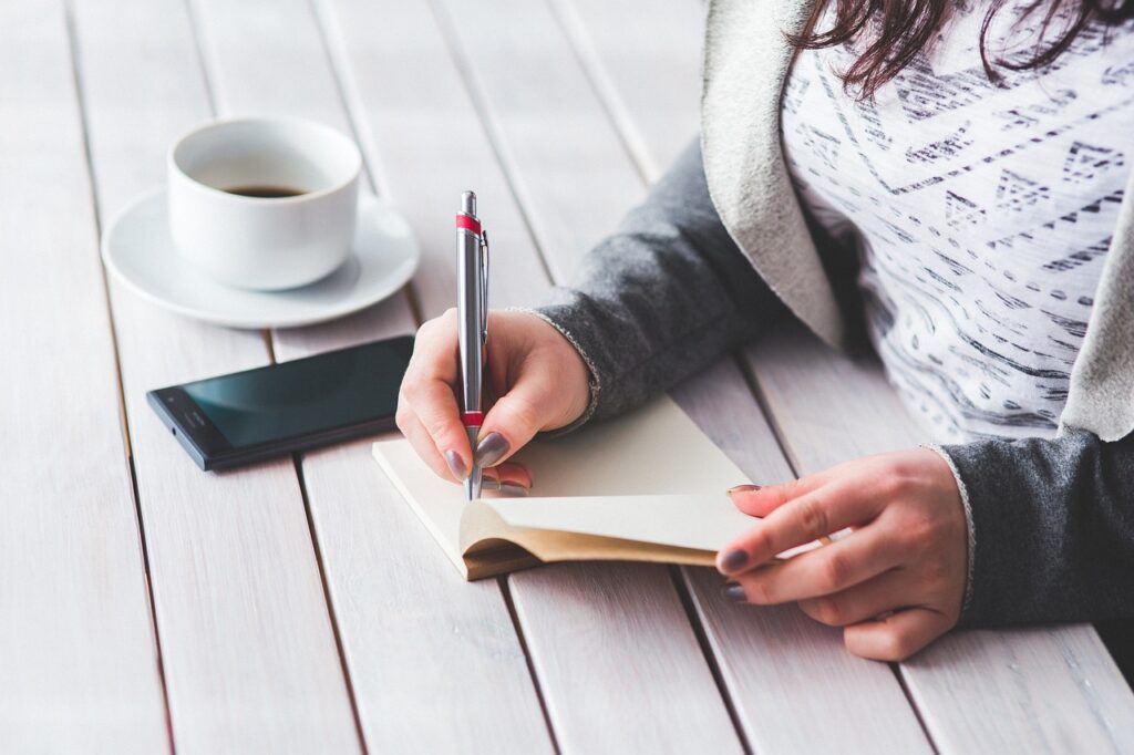 A woman at work with coffee cup writing in her notebook