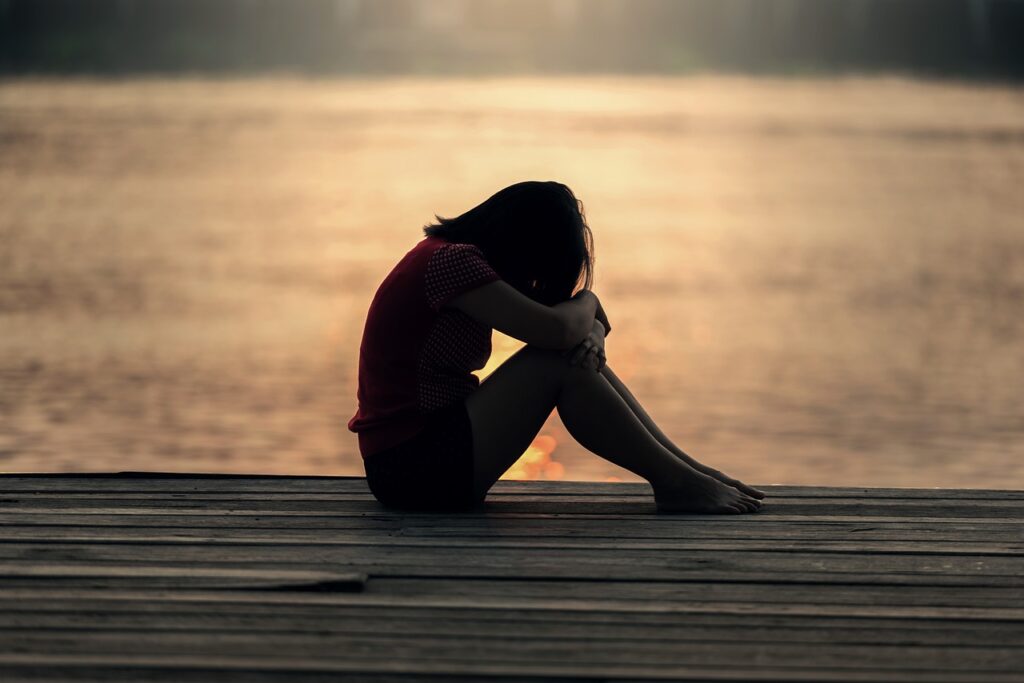 A sad girl sitting against a sunset on a jetty